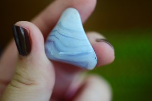 Petite pierre de calcédoine bleue dans les doigts d'une personne pour profiter pleinement des vertus qu'elle dégage.